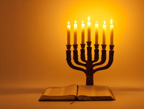 Eine leuchtende Menorah, die in warmem, goldenem Licht erstrahlt und auf einem Tisch steht. Neben ihr liegt eine aufgeschlagene Bibel.